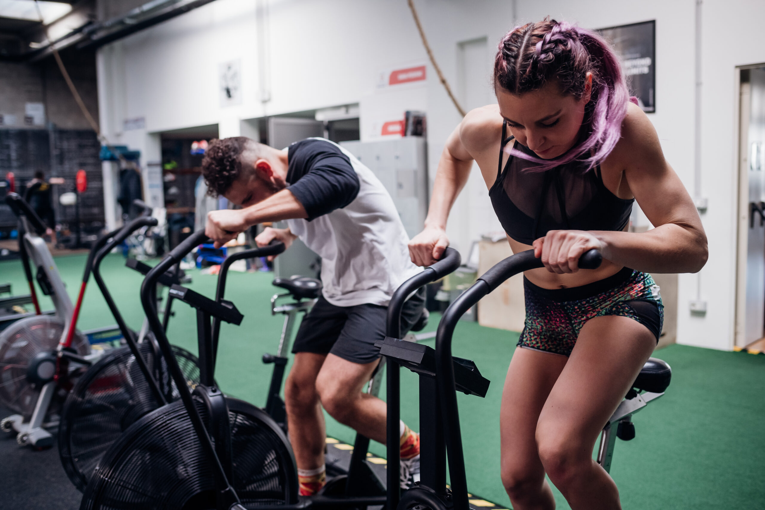 Young woman and man training together on gym exercise bikes, action